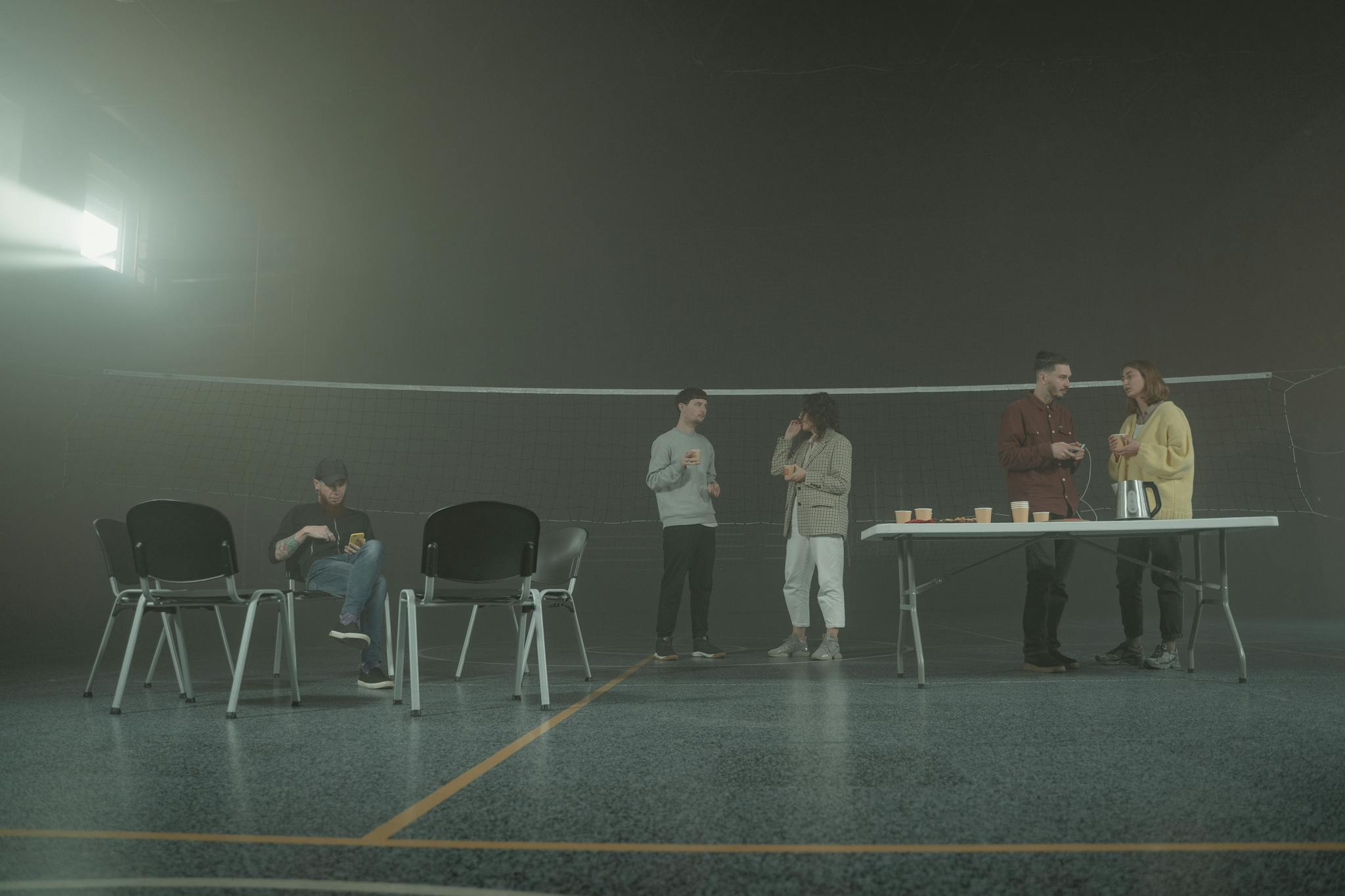 A group of people having a casual discussion in a smoky indoor setting with chairs and a table.