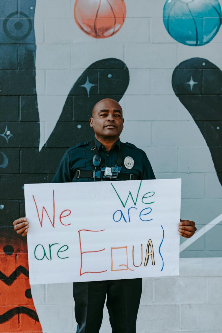 A policeman stands holding an equality sign against a mural backdrop.